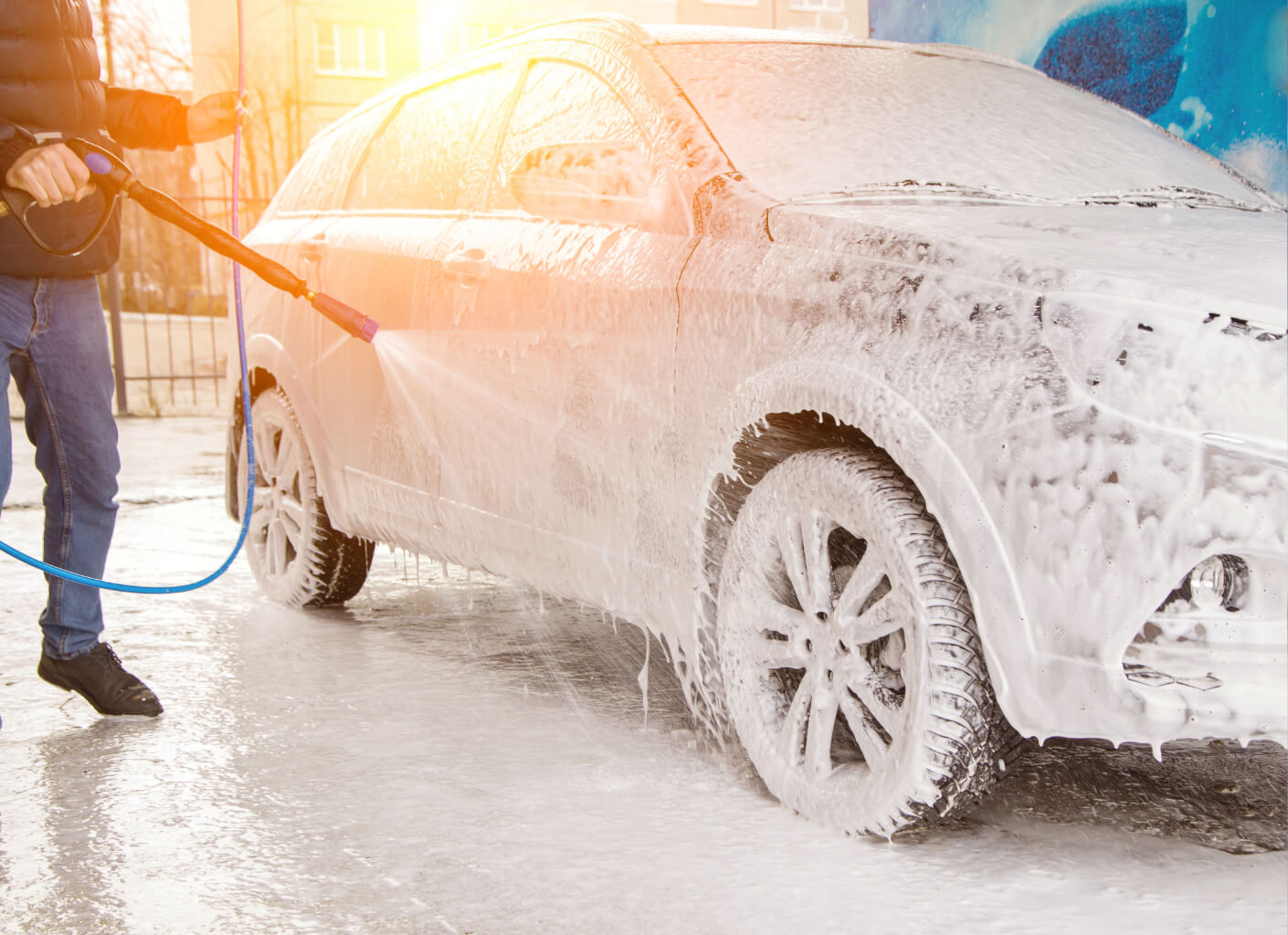 Man using a pressure washer and snow foam on a car during a wash.