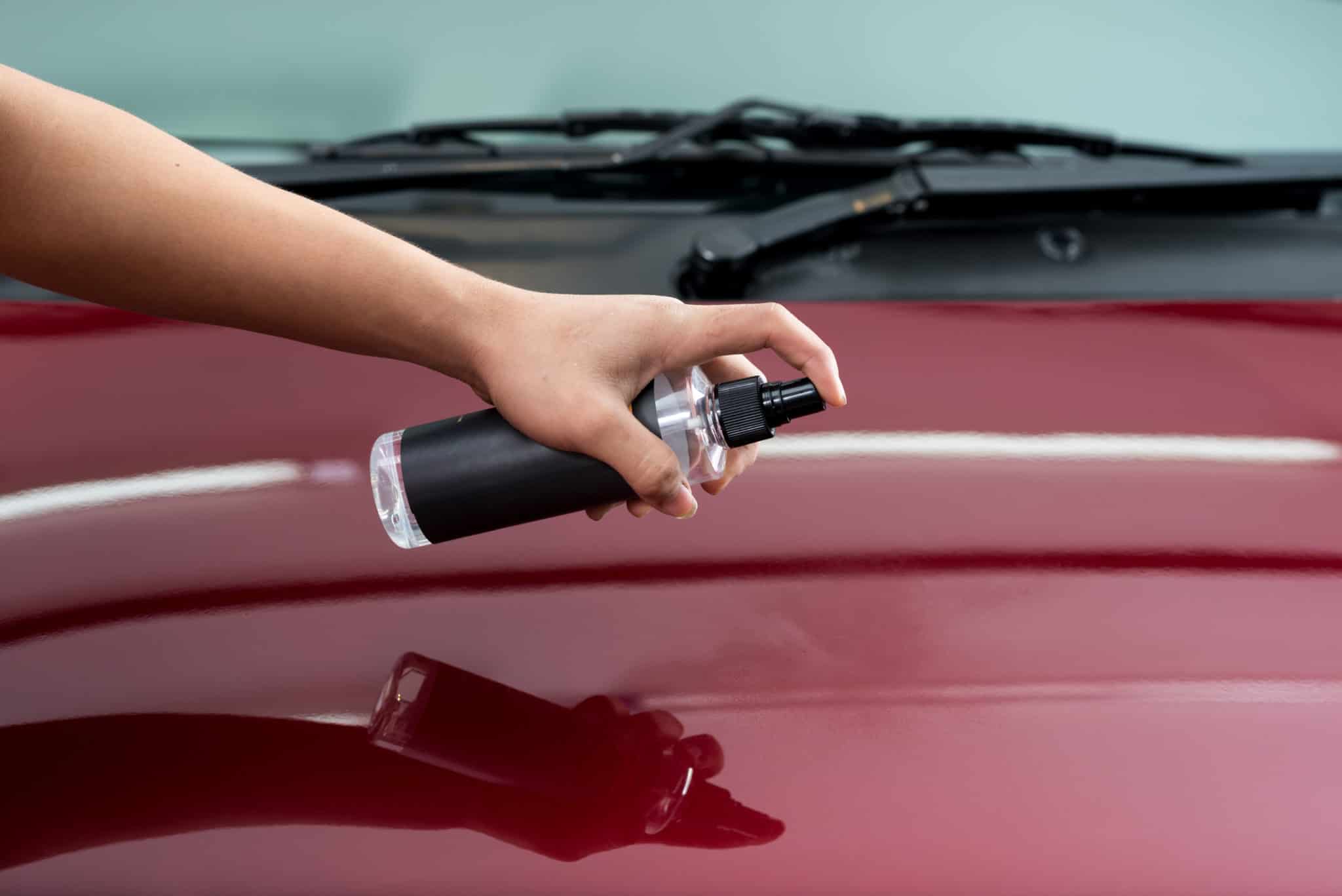 Hand applying waterless car wash spray on a red car bonnet for a shiny finish