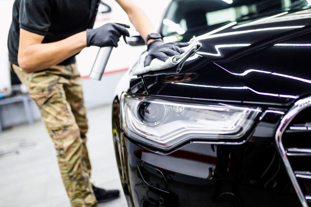 Man using a car detailing kit to clean a black car's bonnet.