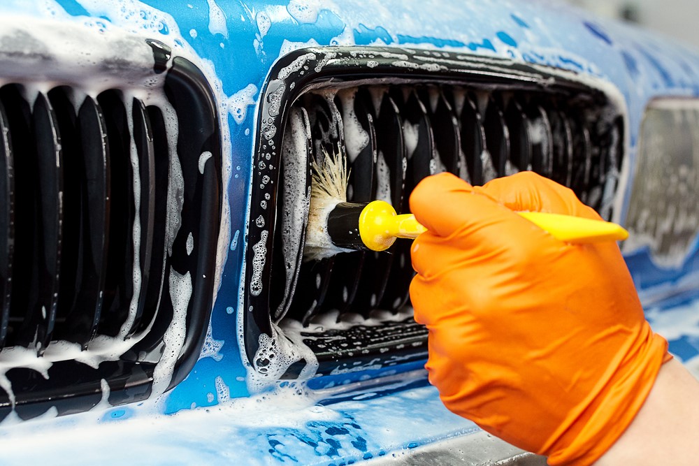 Person using a car detailing brush on a car grille with soap