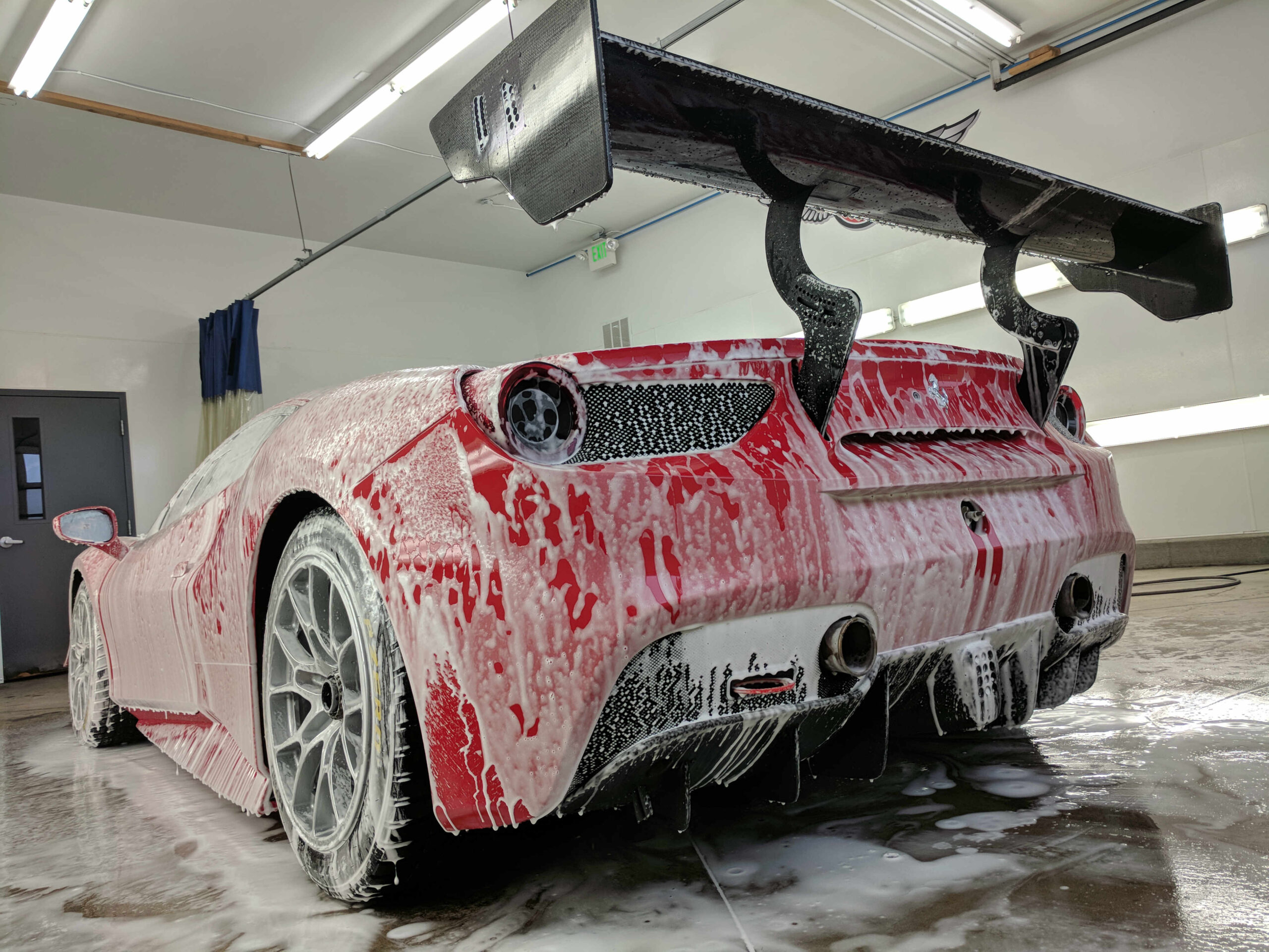 Red sports car covered in foam during pre-wash in a professional car wash facility