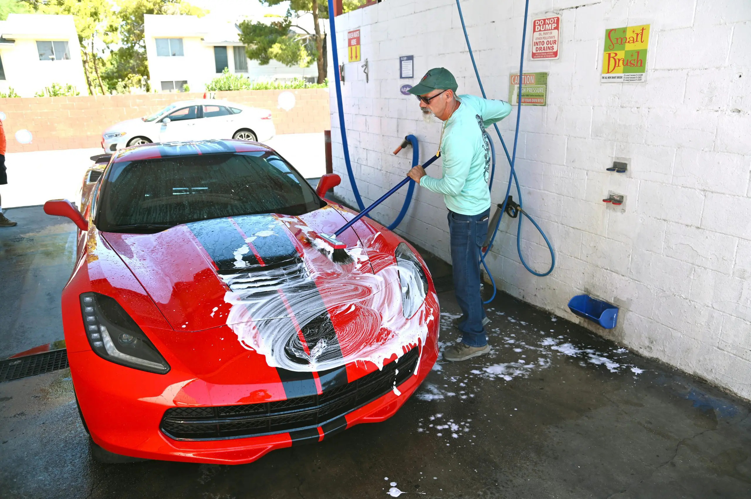 Man washing a red sports car at a self-service car wash station