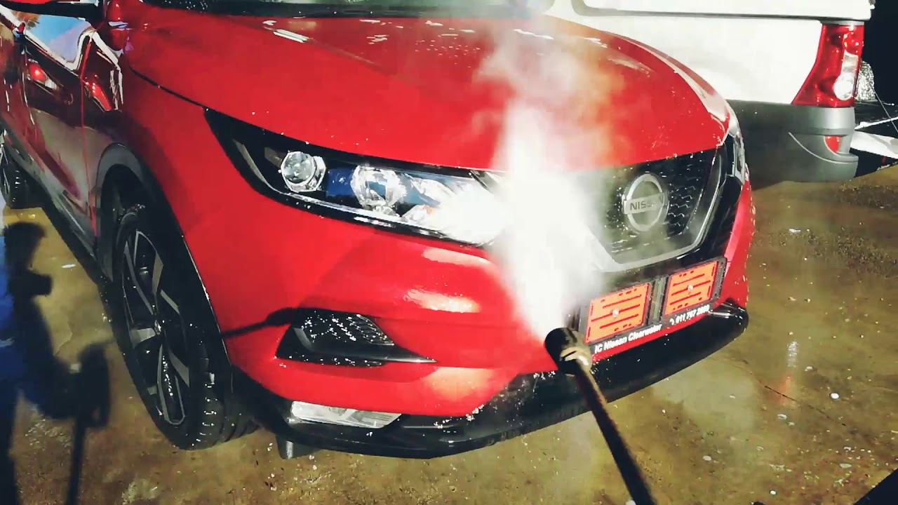 Red car undergoing a steam cleaning process, illustrating the comparison between steam cleaning and traditional washing methods.