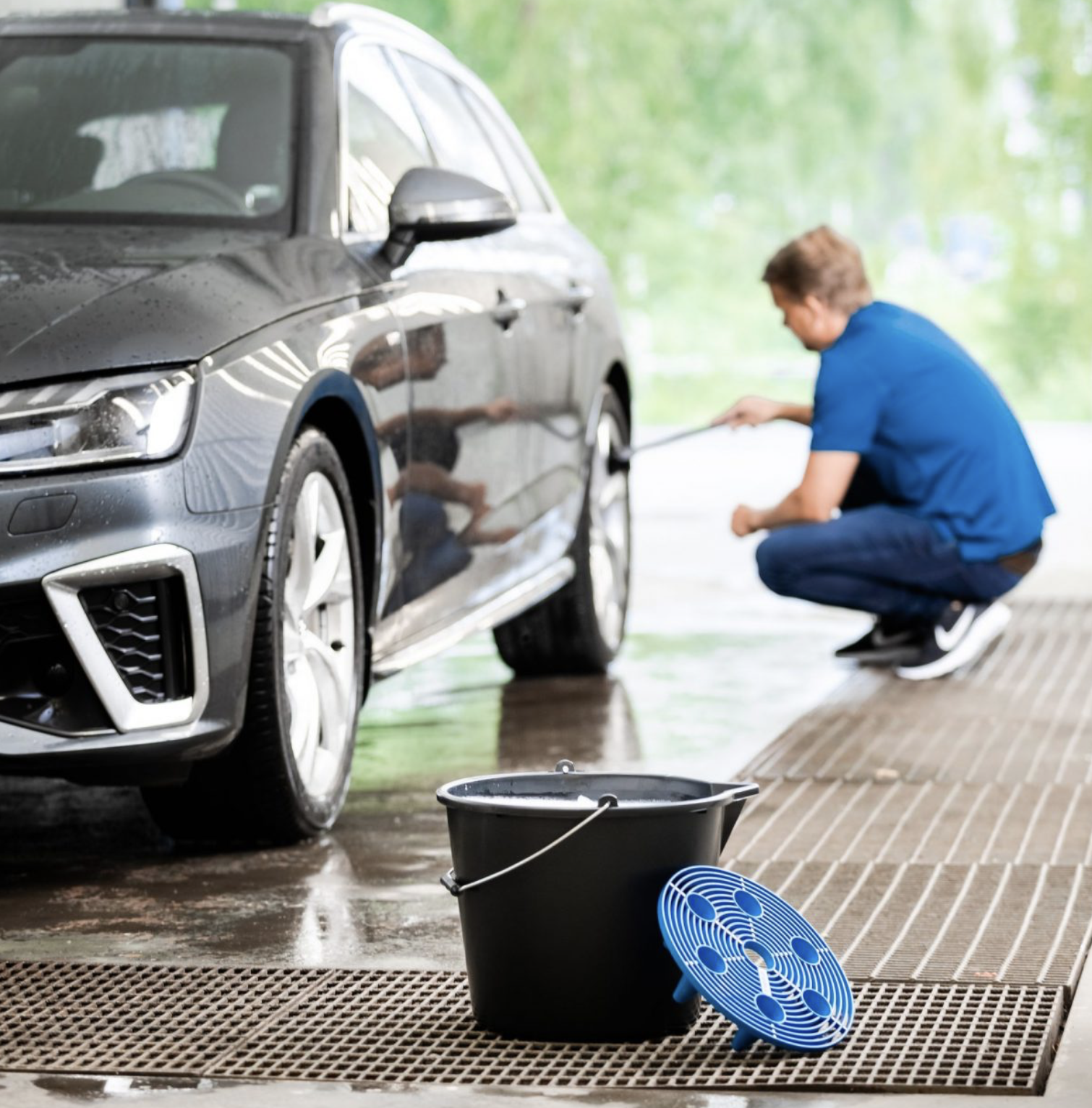 Person using a car wash bucket with a grit guard to clean a vehicle, showcasing its effectiveness in protecting car paint.