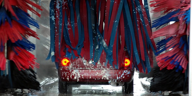 Car inside an automatic car wash with red and blue brushes, emphasizing the safety and standards in UK car wash services.