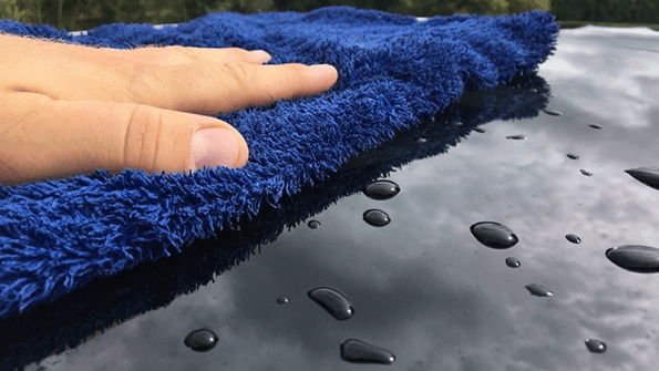 Hand wiping a car's surface with a blue microfiber towel, dispelling common car washing myths for UK drivers.