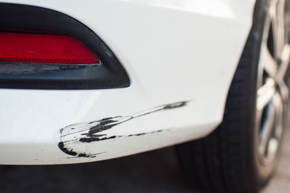 Close-up of a white car with a noticeable black scrape mark, illustrating potential damage from a cheap car wash.