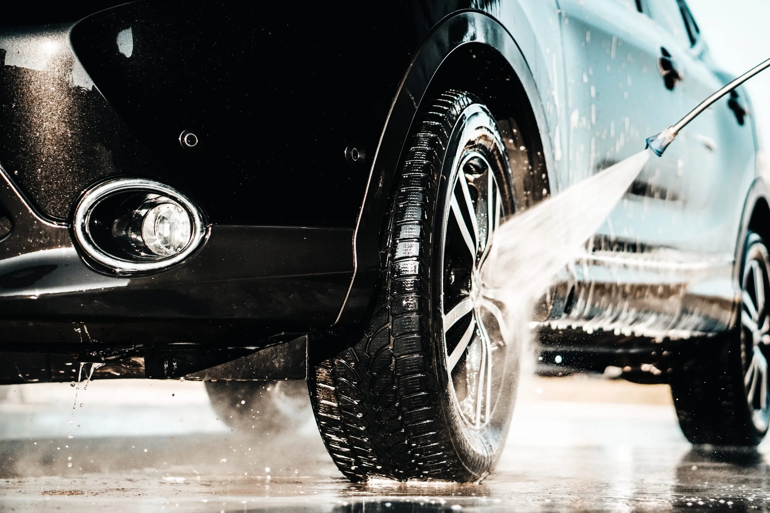 Close-up of a car being washed by hand with high-pressure water, emphasizing the convenience of online booking for hand car wash services in the UK.