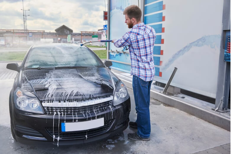 Man washing a car at a self-service car wash station, comparing the benefits and drawbacks of home washing versus self-service in the UK.