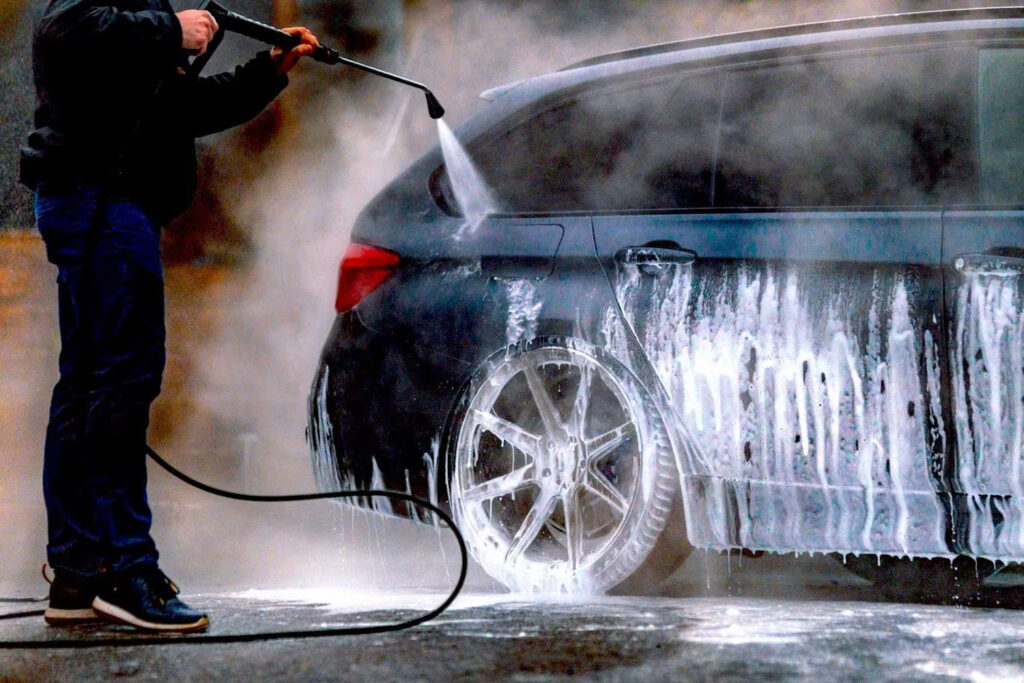 Person using a high-pressure jet wash on a car, demonstrating the ideal car washing schedule for maintaining cleanliness and protection.