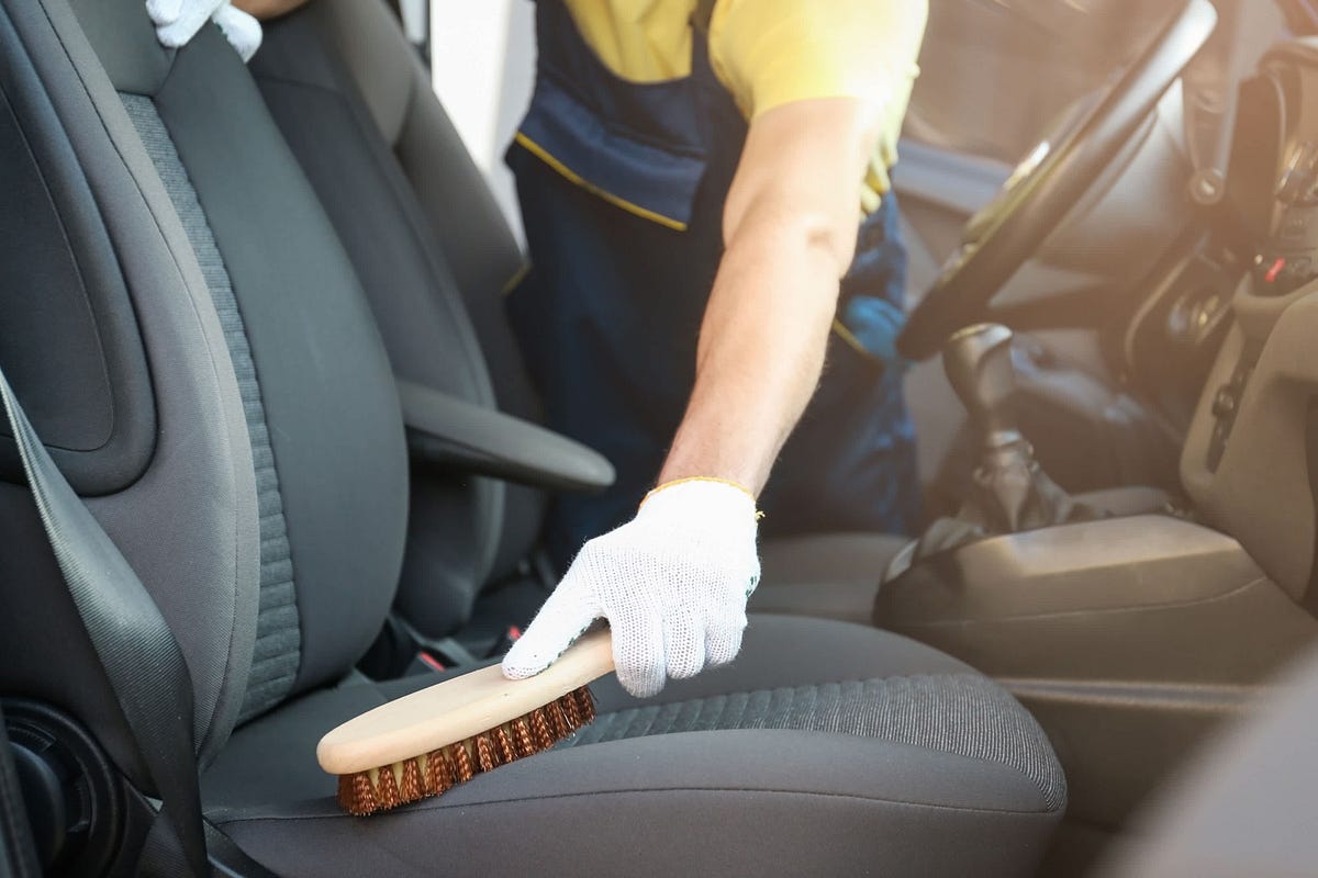 Professional valet cleaning car seats with a brush, ideal for removing pet fur and odours for pet owners in the UK.