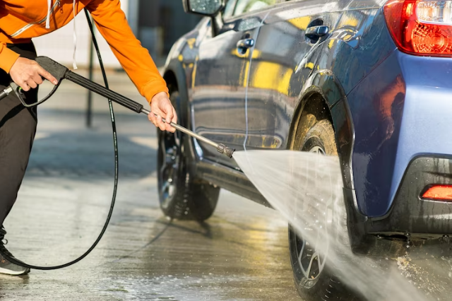 Person using a self-service jet wash on a blue car