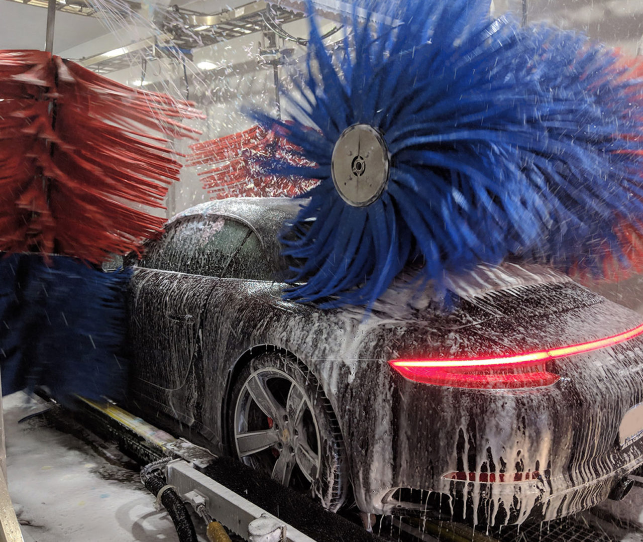 Car inside a drive-through car wash with red and blue brushes, illustrating the potential risks and benefits of automated car washing services.