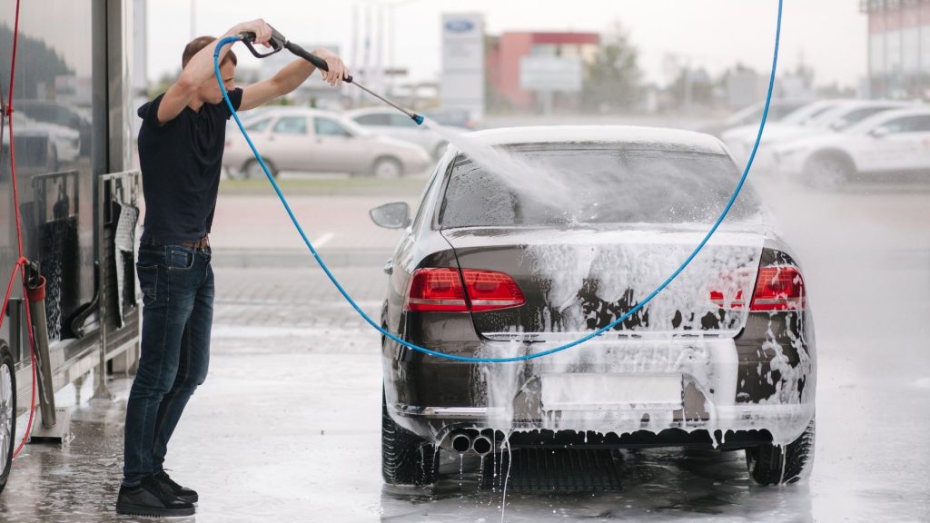 Man washing a car at a petrol station with a high-pressure hose