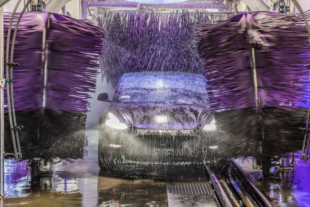 Car going through a drive-through car wash with purple brushes, illustrating the limitations of automated car washes compared to hand washing.